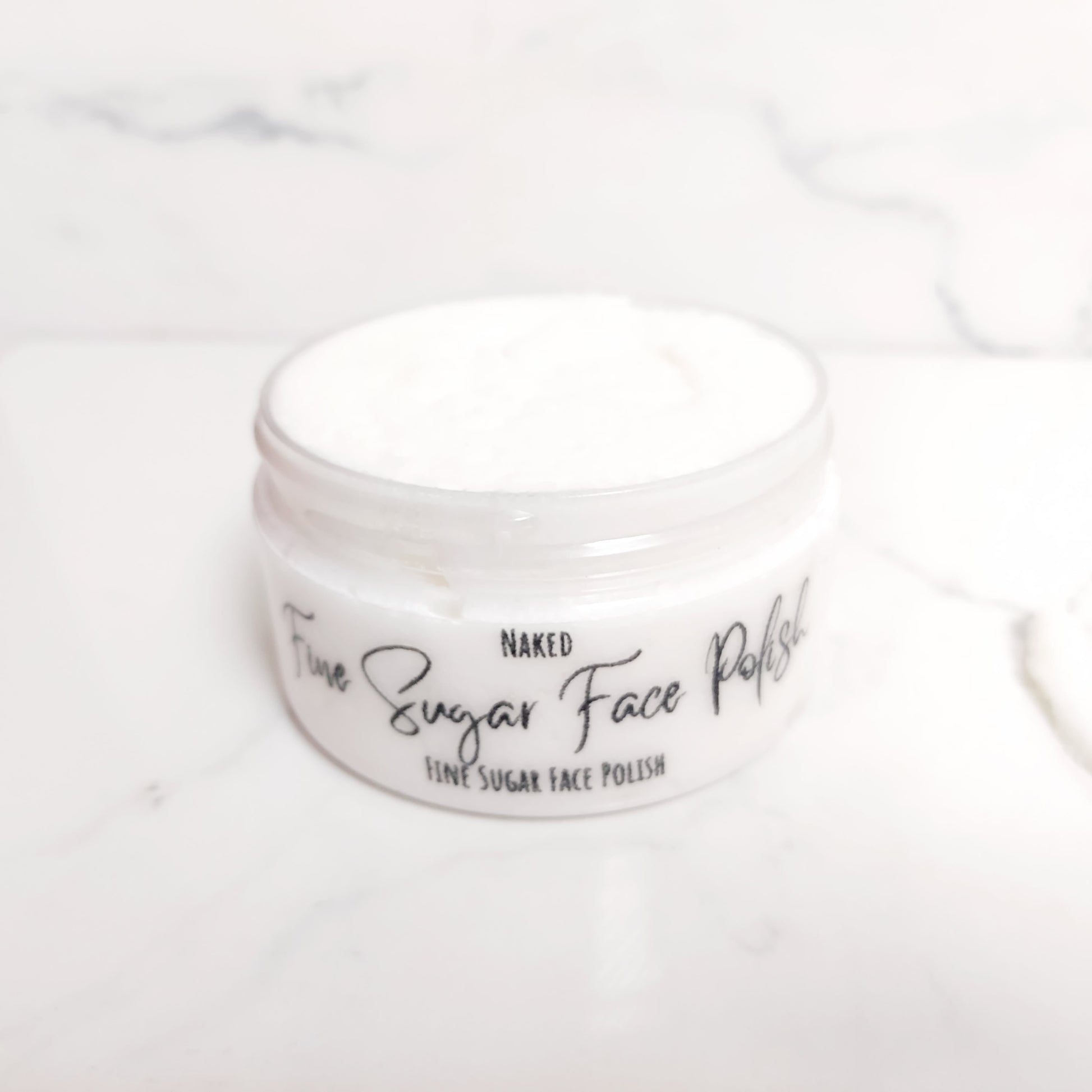 Fine sugar face polish, caster sugar face scrub, face scrub, clear short tub showing a bright white face polish paste. Cosmetic Oils and butters with caster sugar face scrub. 